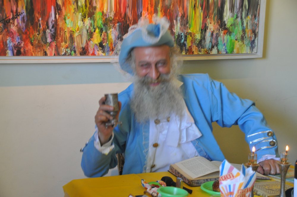 Yoel Tordjman at the Purim table, one of his own paintings on the wall behind him